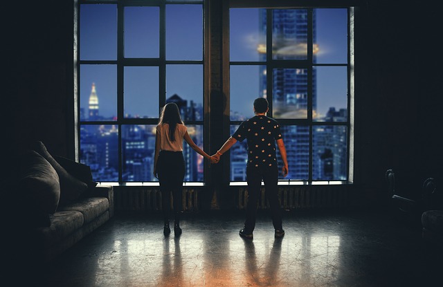 Muž a žena stoja pred veľkými oknami a držia sa za ruky